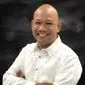 Smiling bald man in a white chef jacket against a dark background