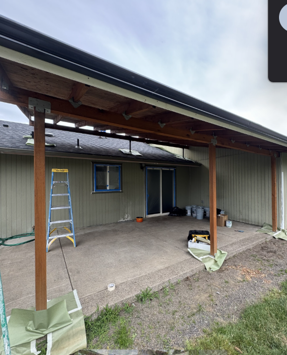 Worker painting the trim of a house roof while standing on a ladder
