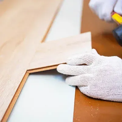 Gloved hands measuring a wooden frame on a workbench