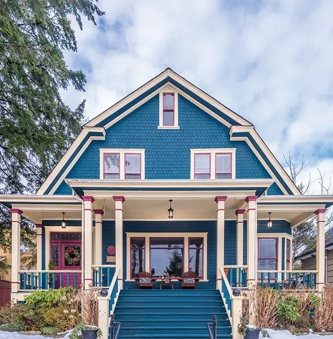 Blue Victorian-style house with white trim, pink accents, and a front porch with steps and columns