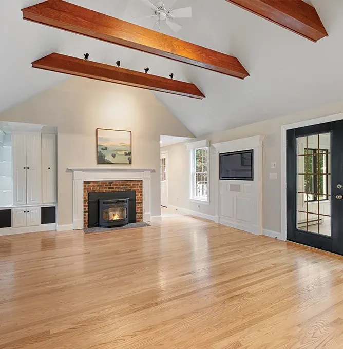 Bright living room with wood floors, exposed ceiling beams, fireplace, and large windows