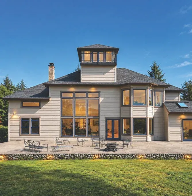 Modern gray house with large windows, a porch, and a manicured lawn in front