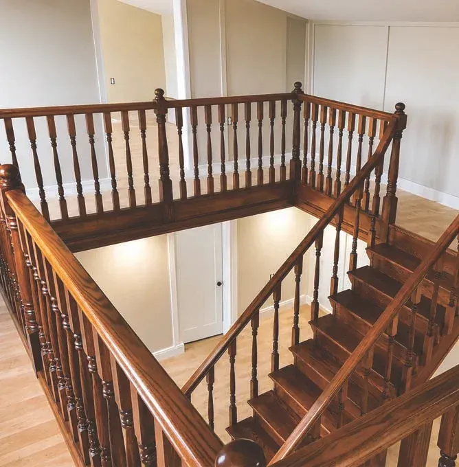 Wooden staircase with railings surrounding an open landing in a bright interior hall