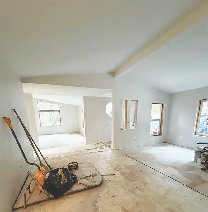 Empty, unfinished room with bare floors, white walls, and windows; cleaning tools in the foreground