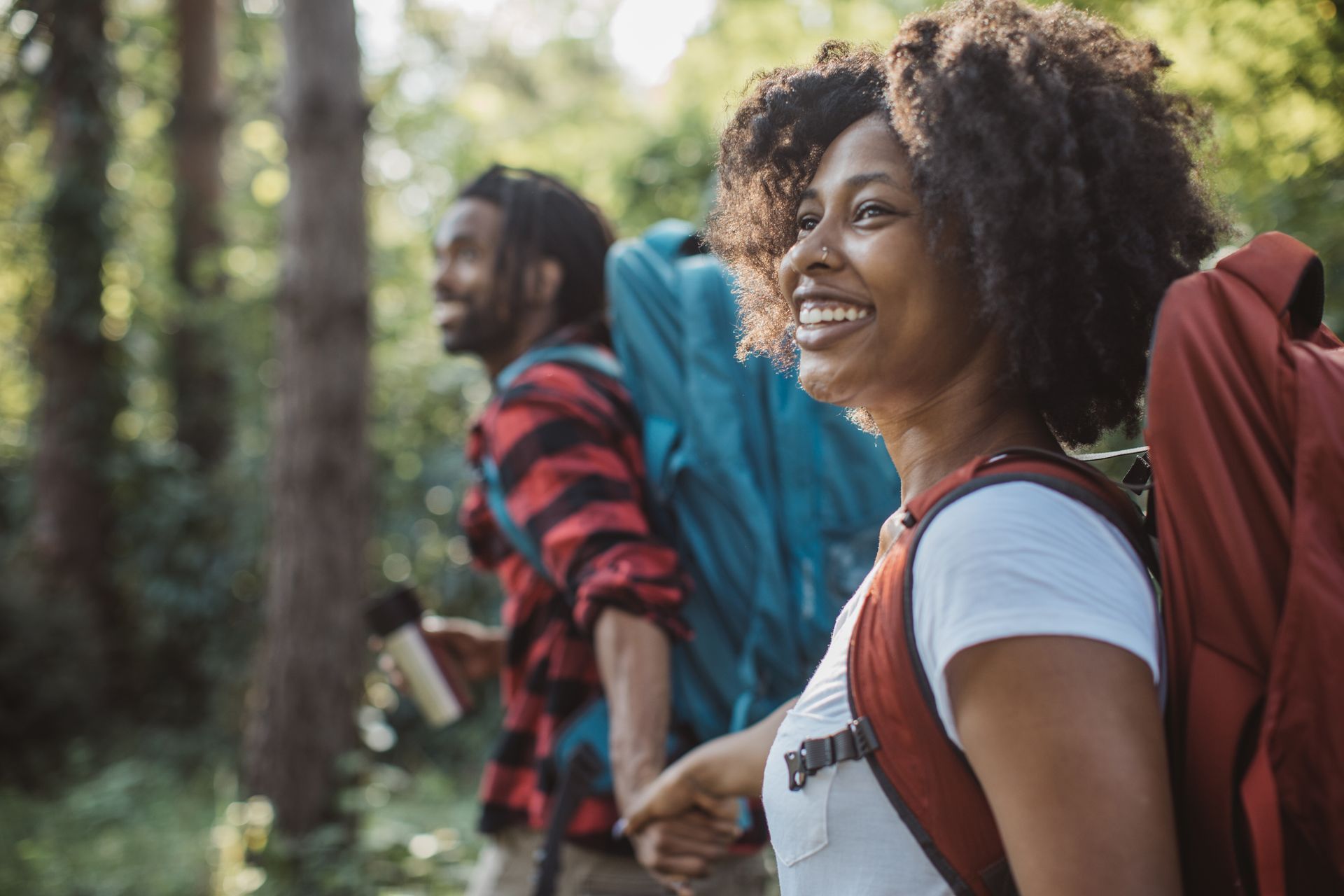 A man and a woman are hiking in the woods with backpacks.