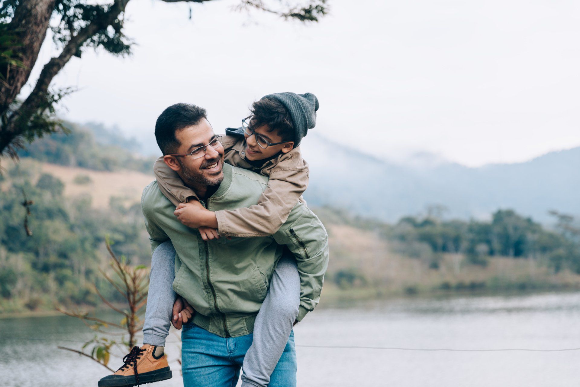 A man is carrying a child on his back near a lake.