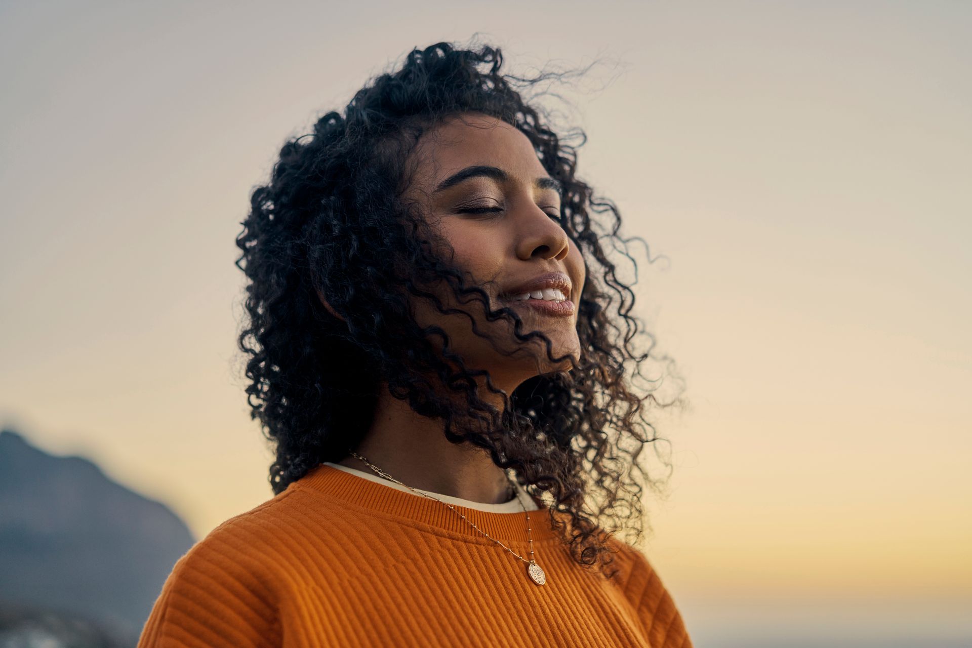 A woman with curly hair is standing with her eyes closed.