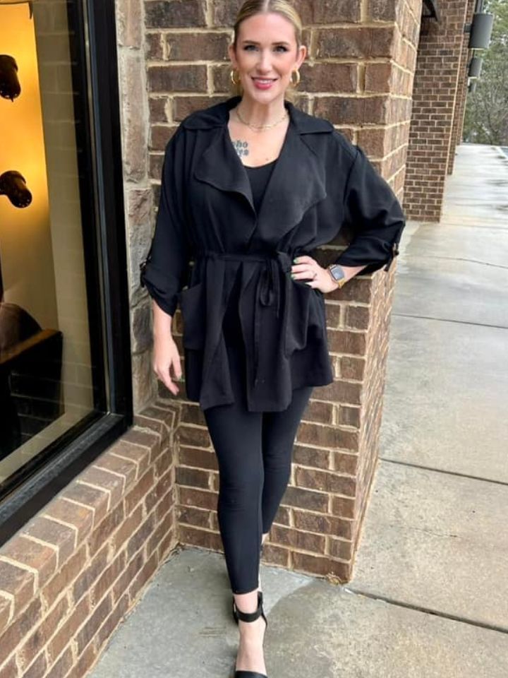 A woman in a black coat and leggings is standing in front of a brick building.