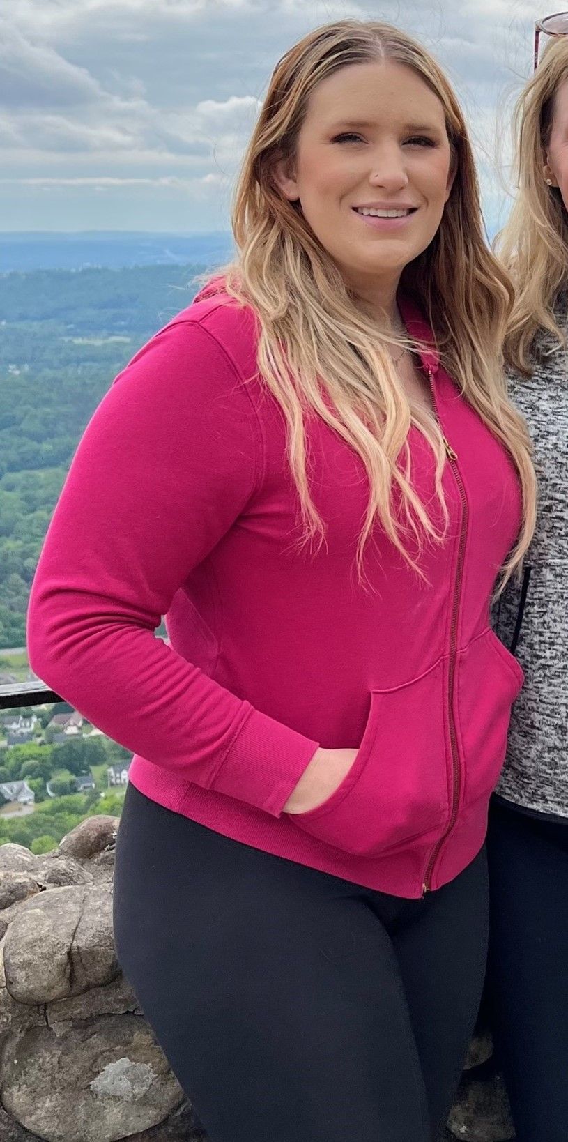 A woman in a pink jacket and black pants is standing next to another woman.