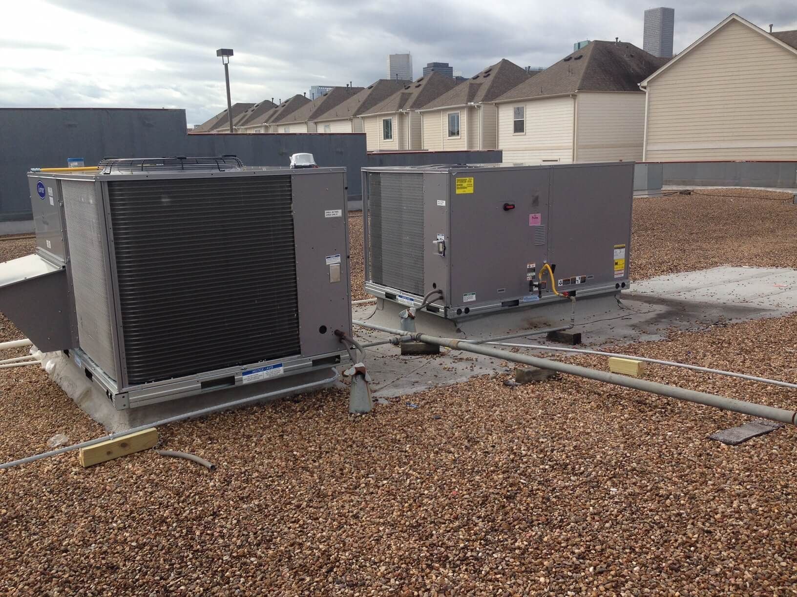Two air conditioners are sitting on top of a gravel roof.