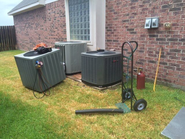 Two air conditioners are sitting on the grass in front of a brick building.