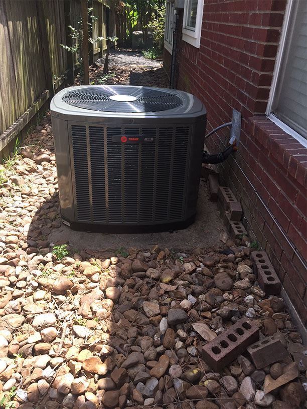 An air conditioner is sitting on the side of a brick house.