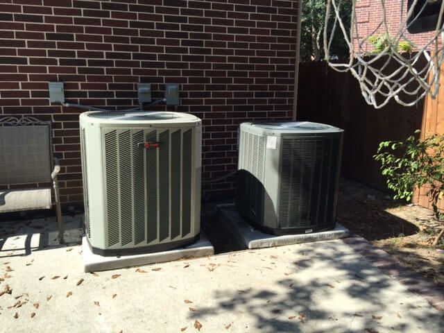 Two air conditioners are sitting outside of a brick building