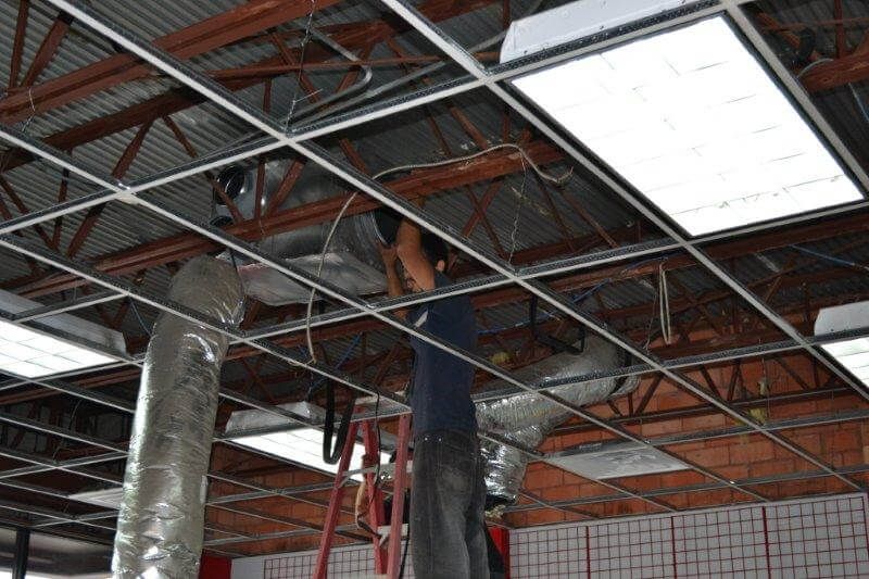 A man is standing on a ladder working on the ceiling of a building.