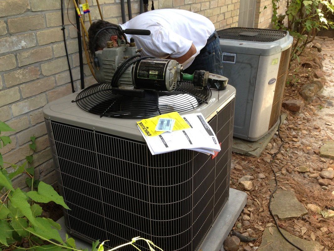A man is working on an air conditioner outside of a brick building.