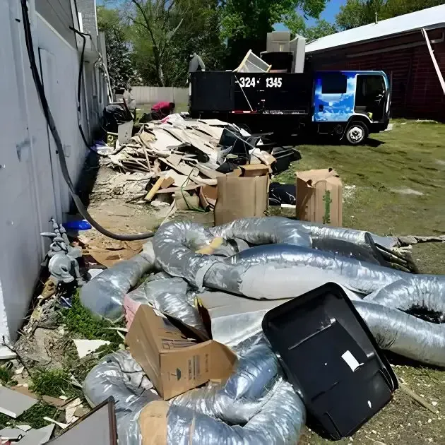 Debris, collapsed ducting, and trash piled beside a building, with a blue truck in the background.
