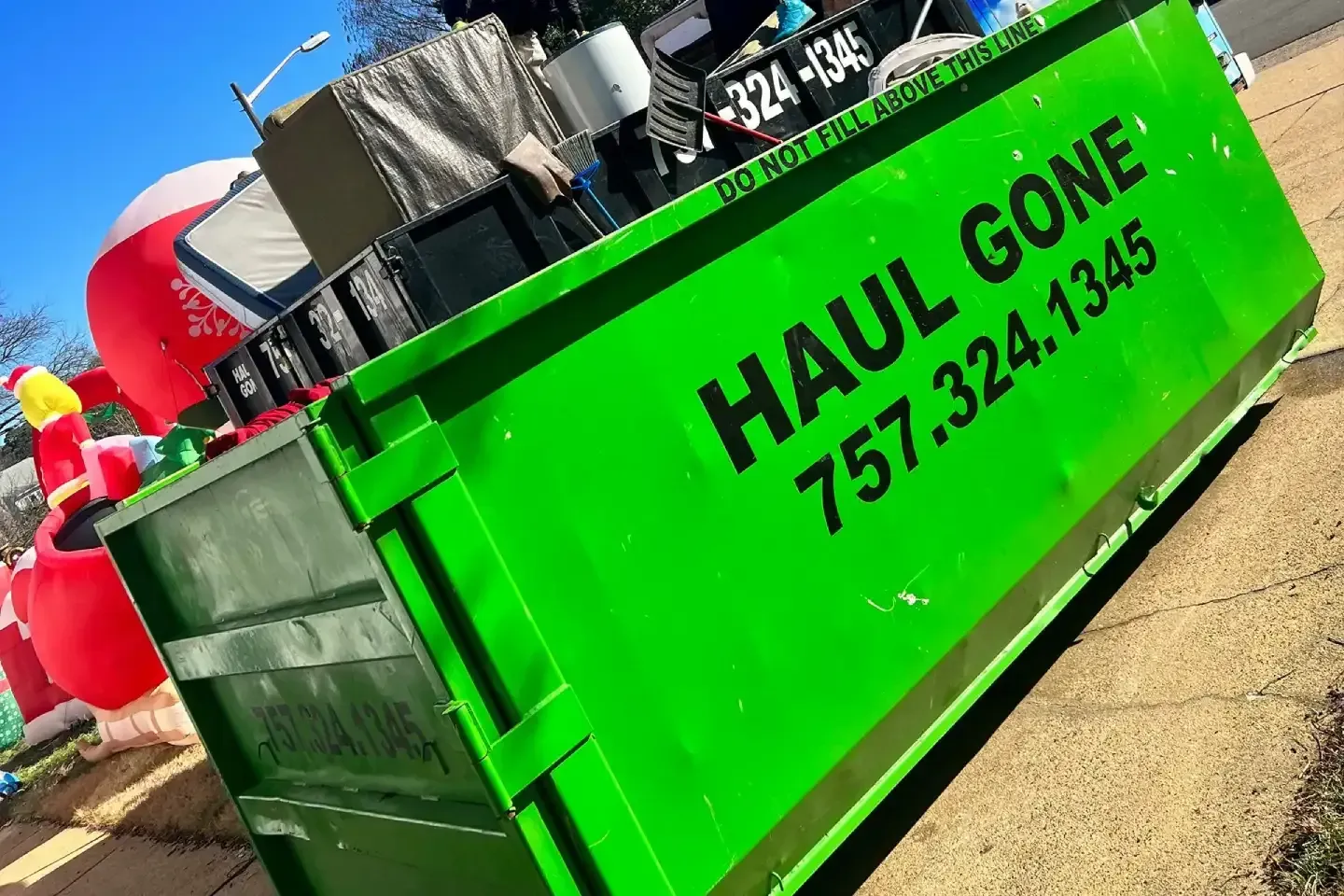 Bright green Haul Gone dumpster with black text and trash inside, outdoors in sunlight