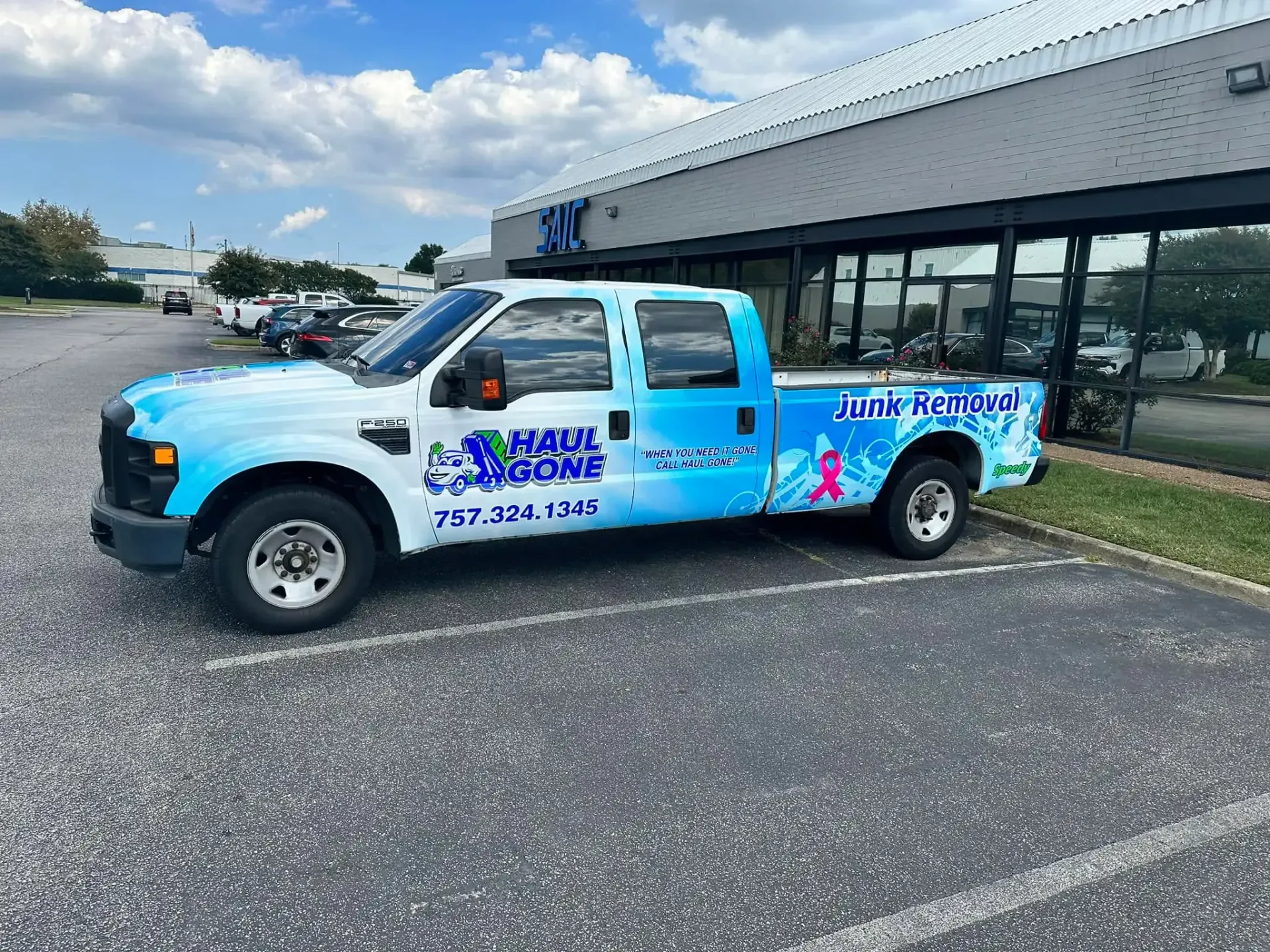Blue and white service truck with company graphics parked outside a building under a cloudy sky