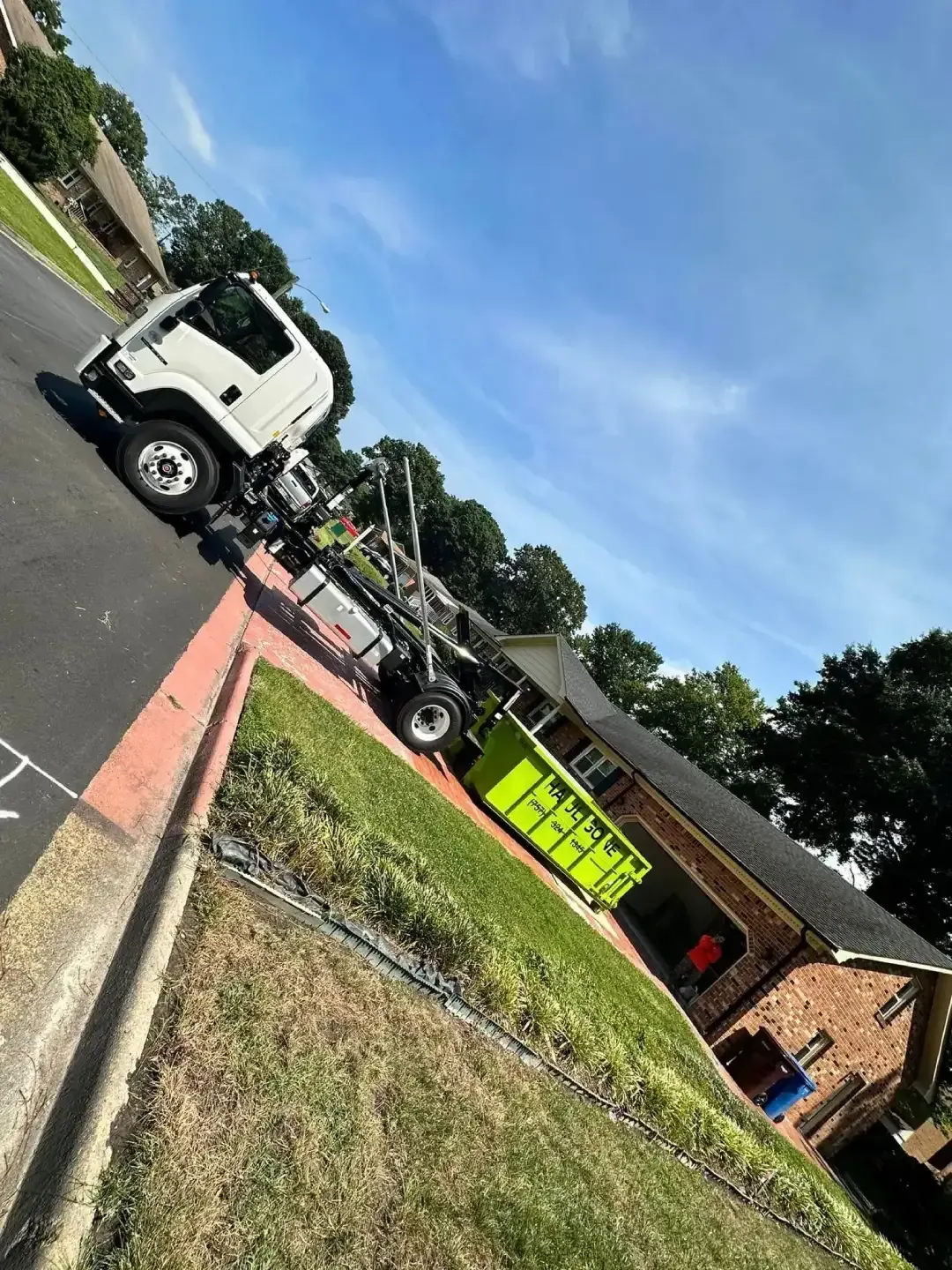 Tow truck loading a bright yellow truck on a roadside near a brick building under a blue sky