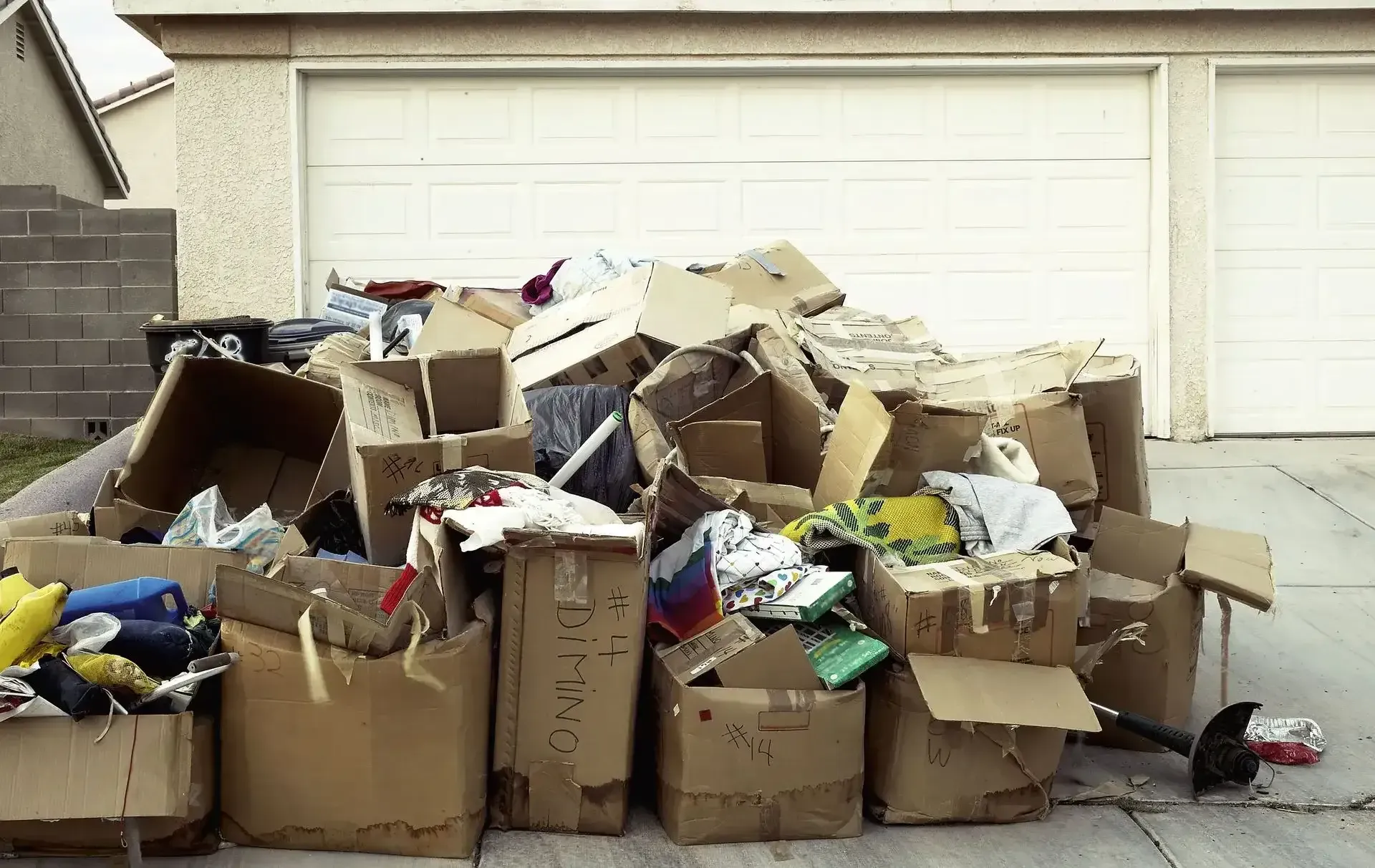 Overflowing cardboard boxes and trash piled in front of a closed garage door
