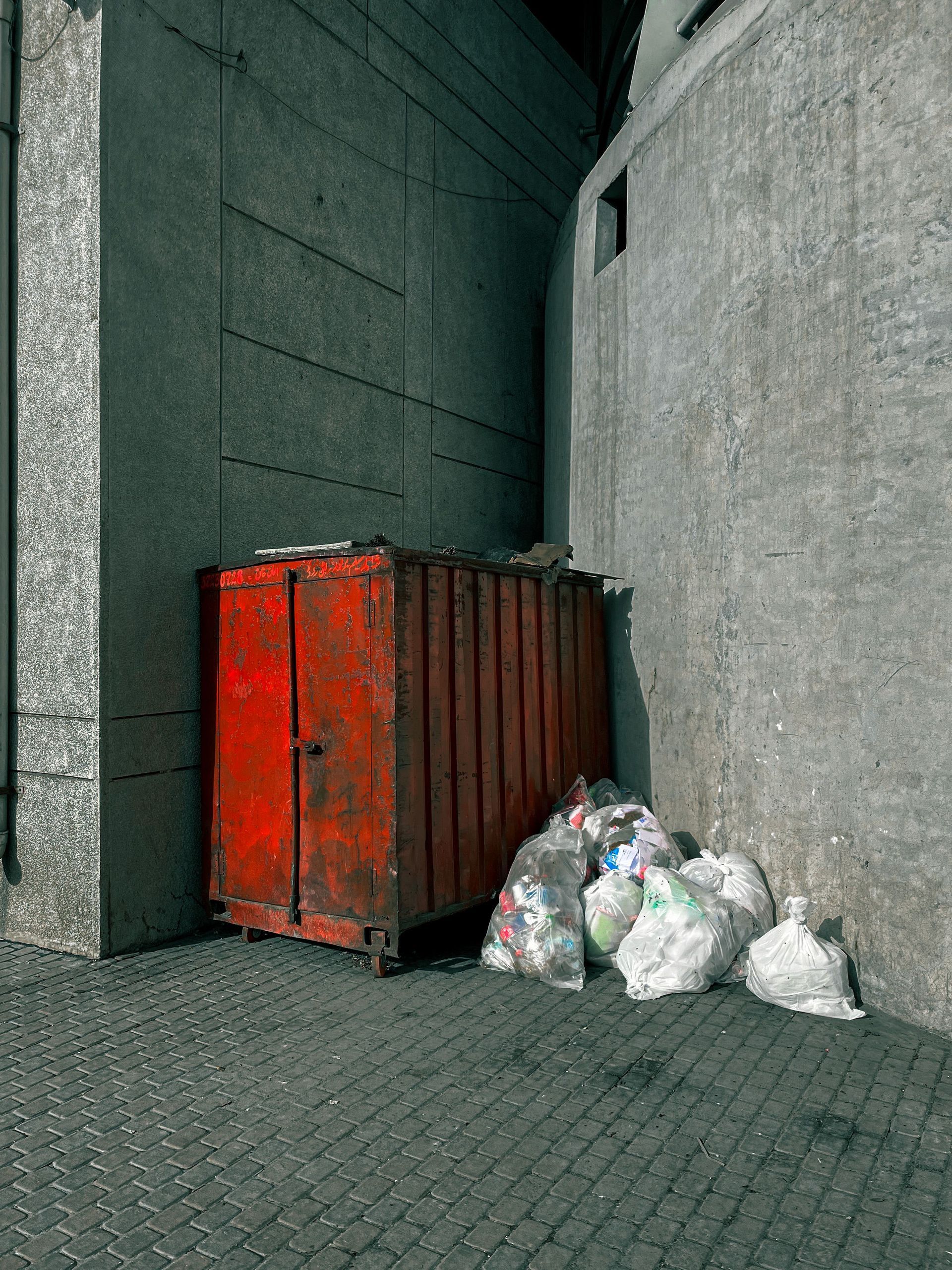 Bright green metal dumpster filled with trash on a street beside a yellow building