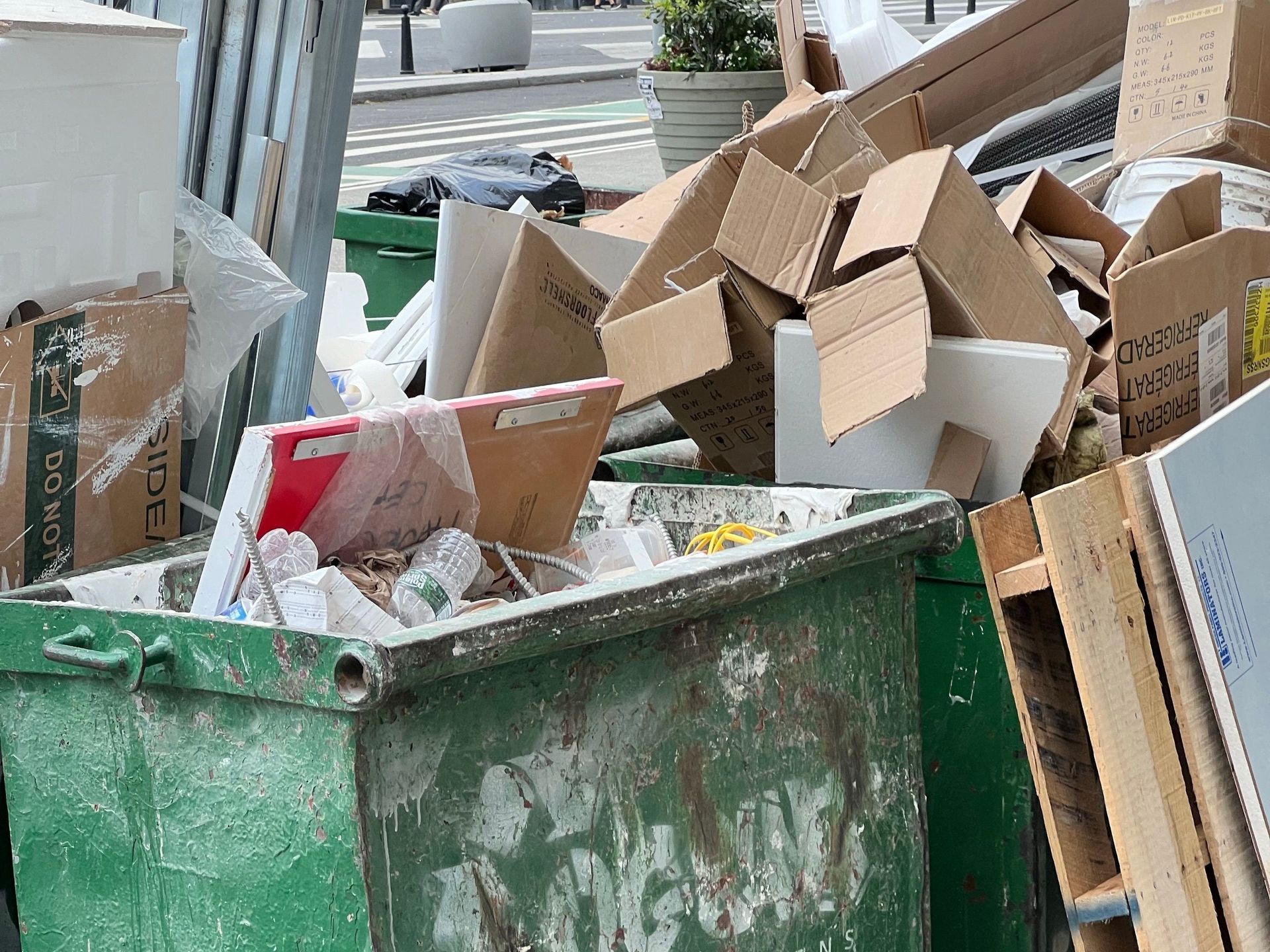 Bright green metal dumpster filled with trash on a street beside a yellow building