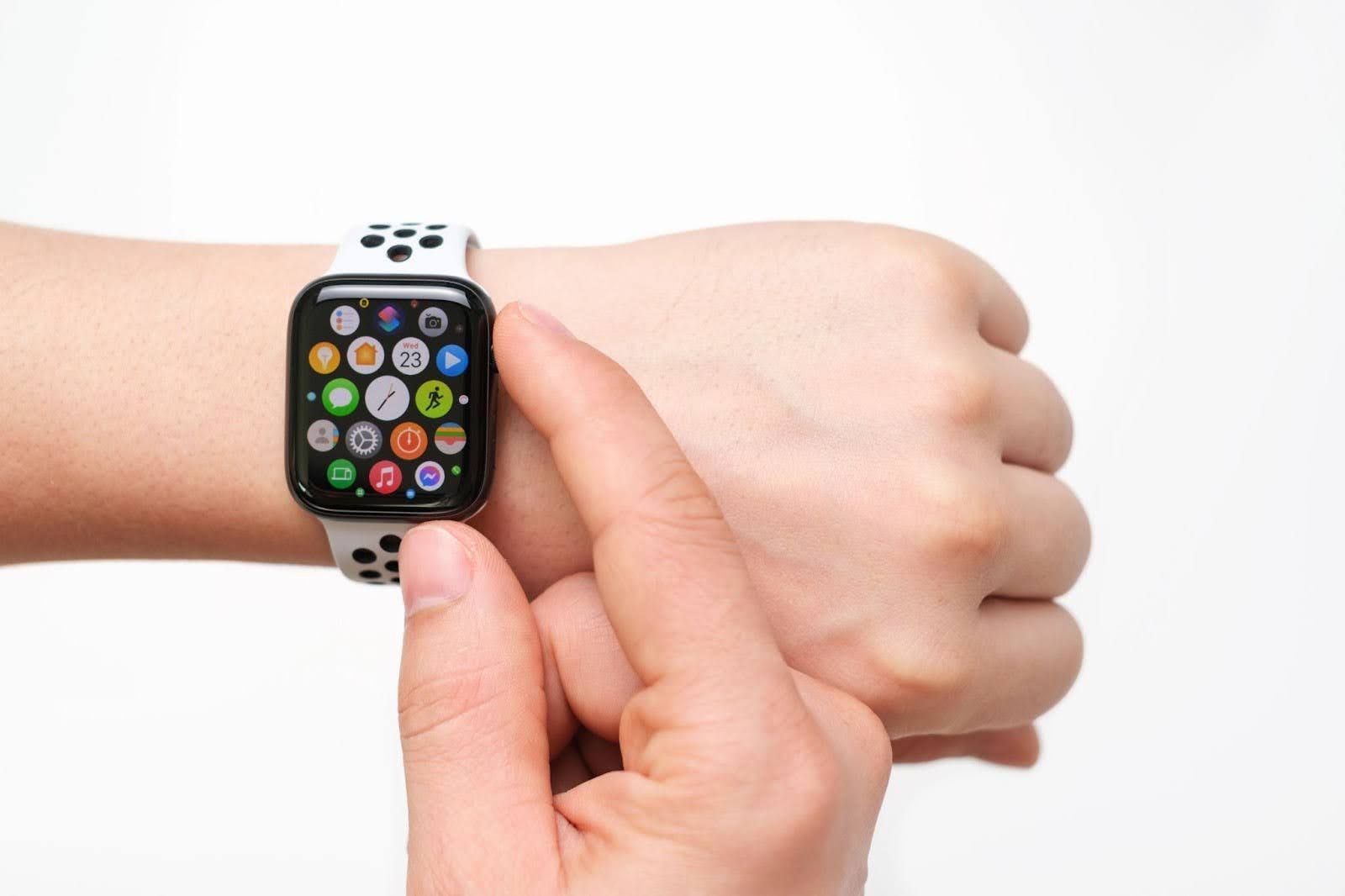A hand taps a smartwatch displaying colorful app icons on a wrist.
