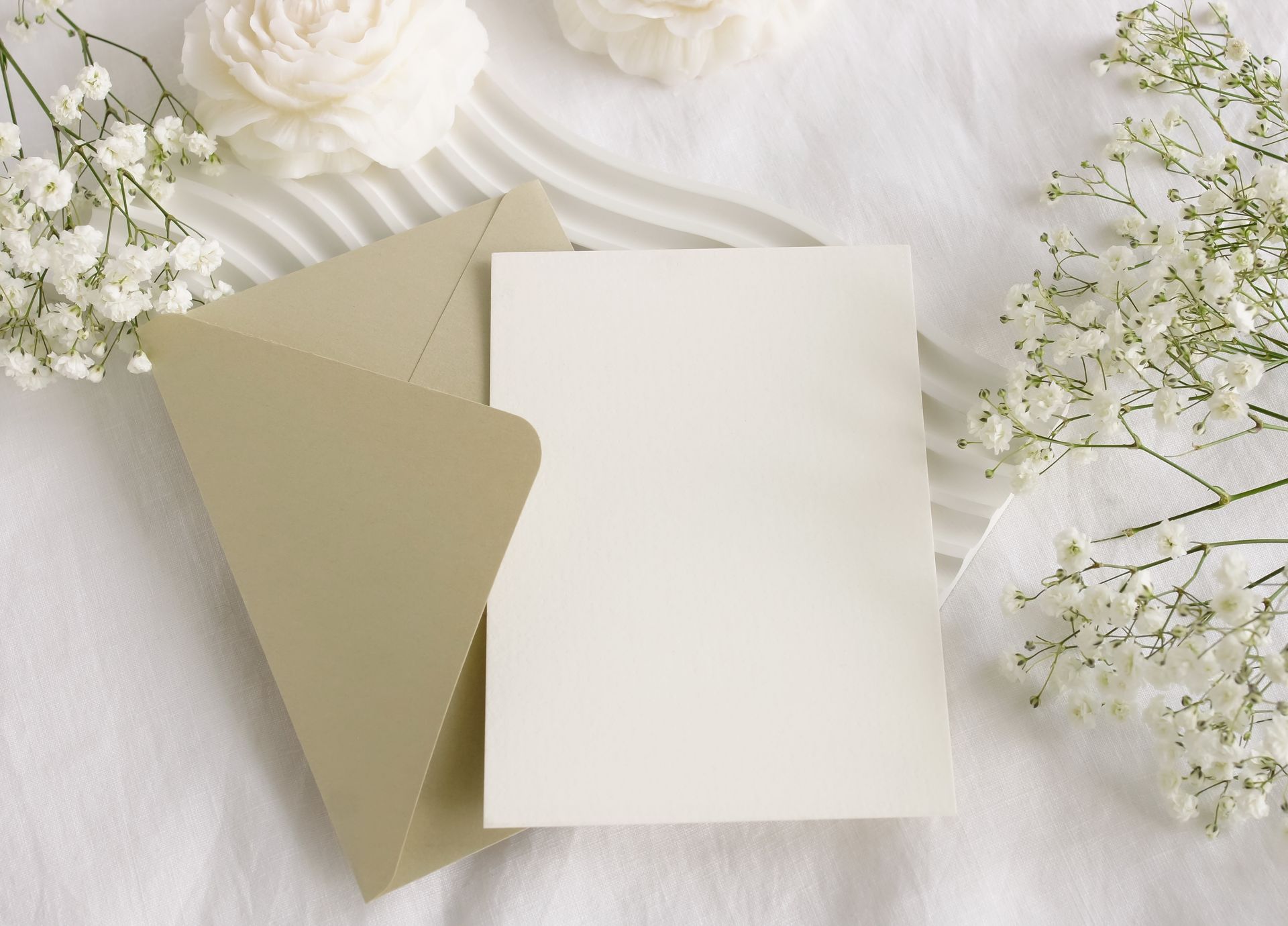 Blank white card with beige envelope on a soft floral background
