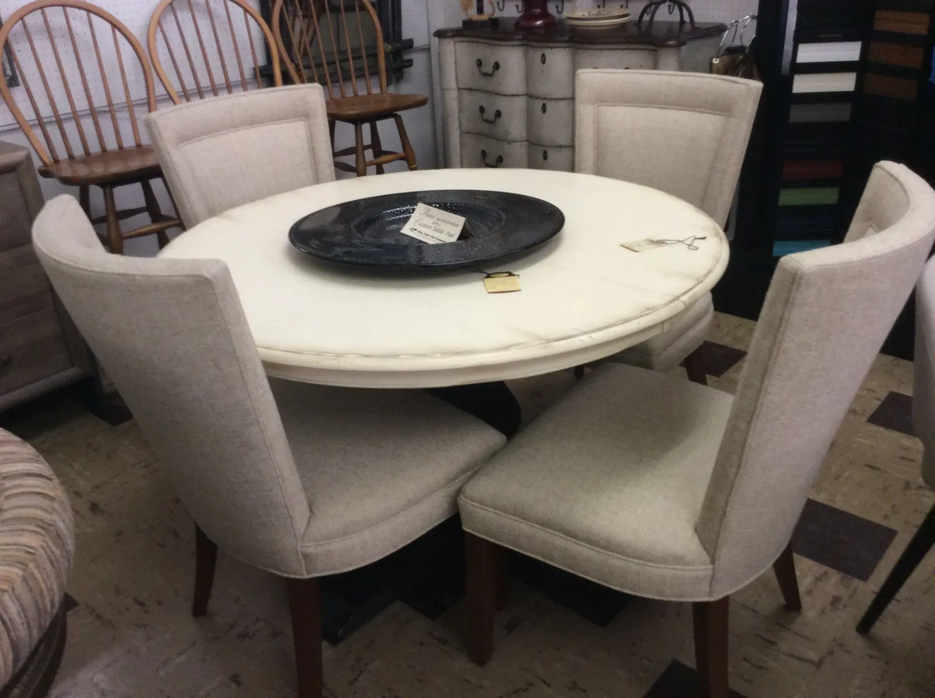 A round, white pedestal dining table set with four upholstered, beige chairs in a furniture showroom.