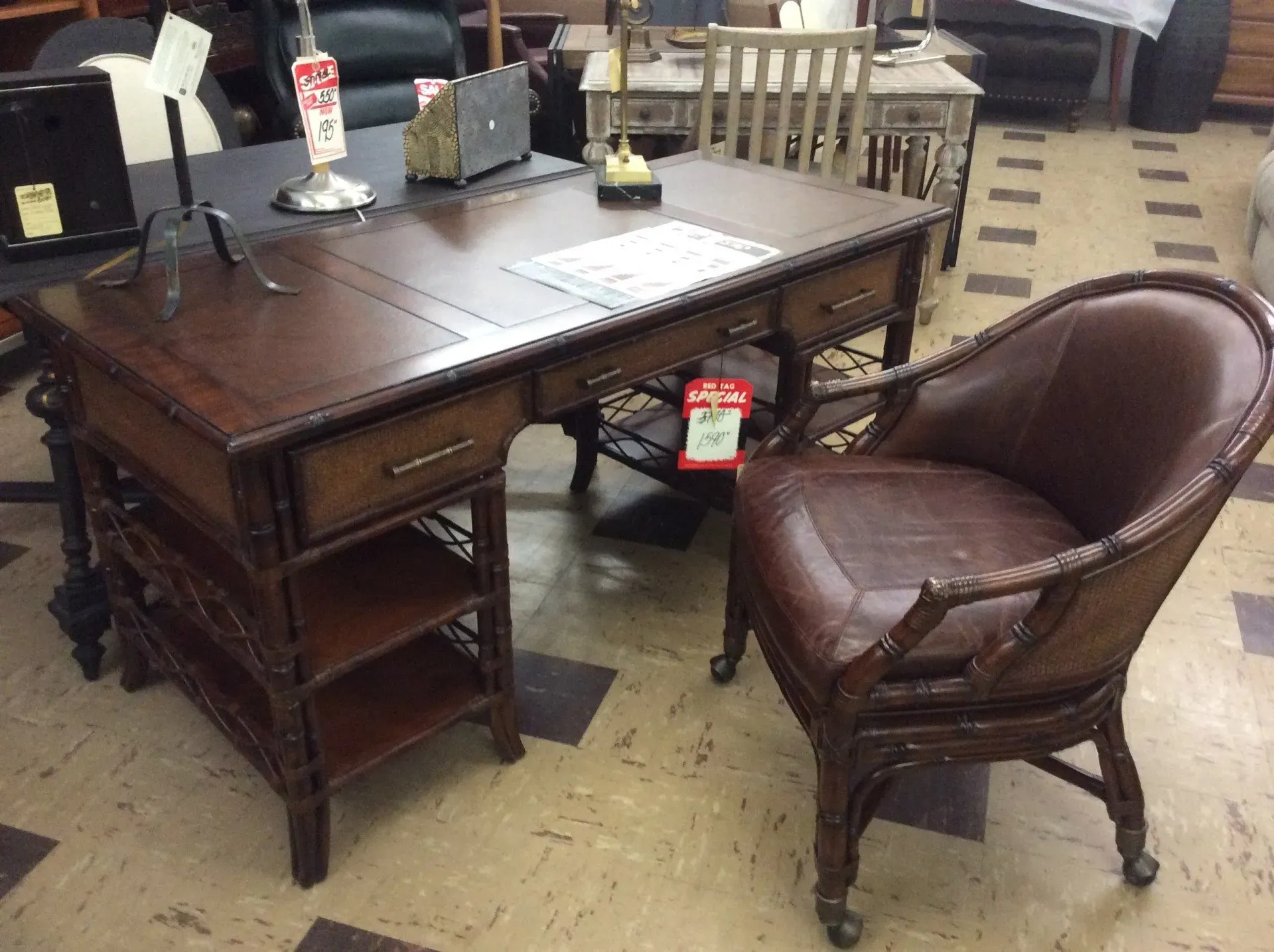 A dark wood desk with side shelving and a matching leather chair on casters, situated in a furniture store.