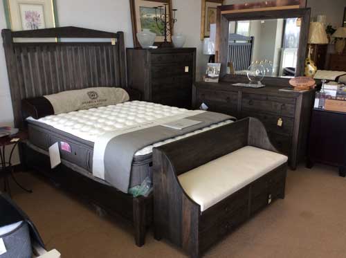 A bedroom set featuring a dark wood bed with a white mattress, a matching dresser with a mirror, and a storage bench.