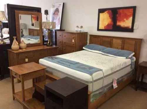 A bedroom display featuring a wooden bed frame, dresser with mirror, chest of drawers, and a small wooden side table.