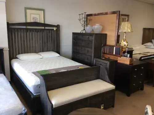 A display of a dark wood bedroom set, including a bed with a bench at its foot, a tall dresser, and a nightstand.