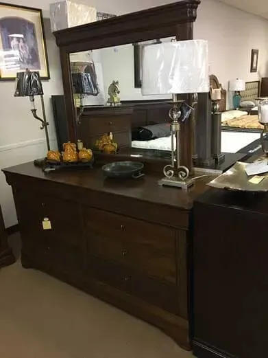 A dark wooden dresser with a matching mirror and a tall lamp sits in a furniture store showroom.