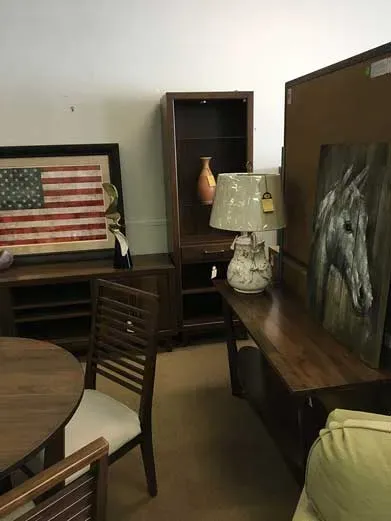 A room with wooden furniture, including a table, chairs, a bookshelf with a vase, and a console table with a lamp.