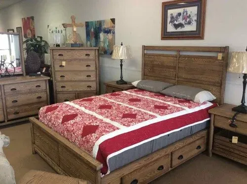 A wood bedroom set featuring a storage bed with a red and white quilt, a tall dresser, and a matching nightstand.