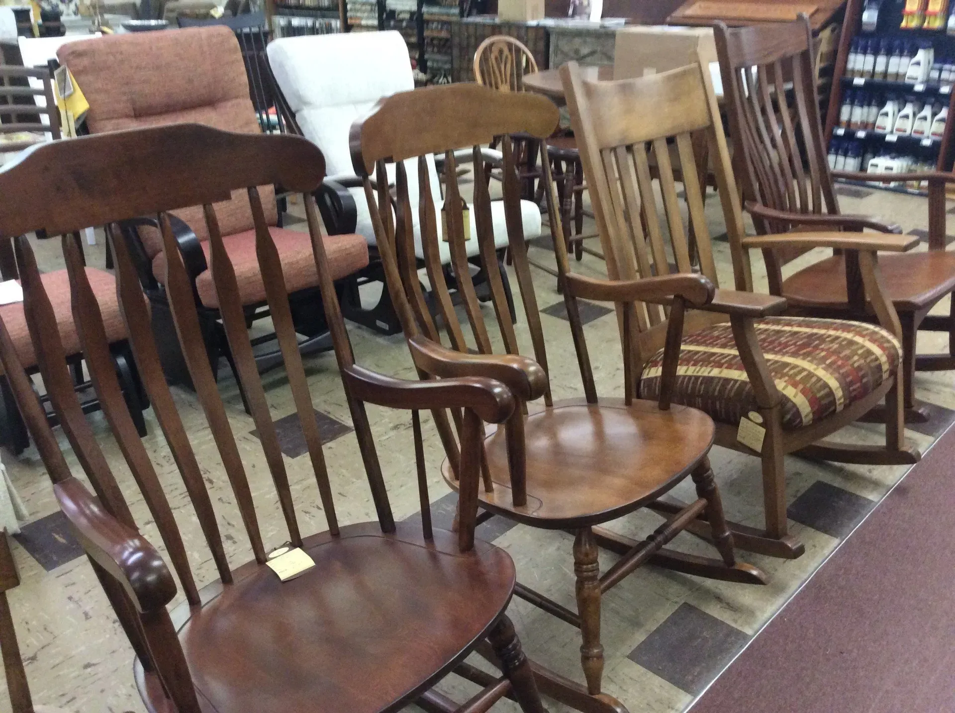 A row of wooden rocking chairs in a furniture store, with upholstered chairs visible in the background.