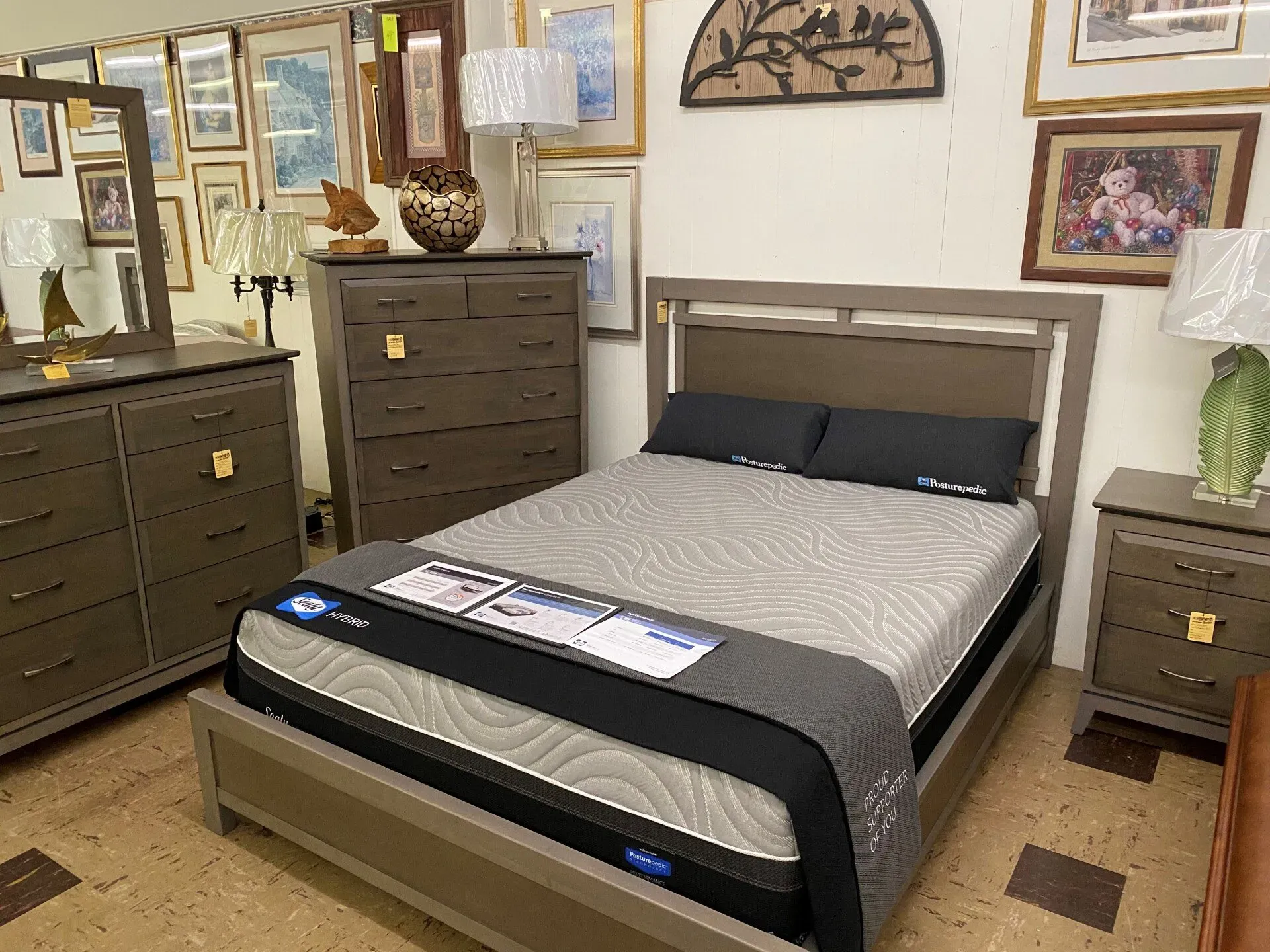 A bedroom furniture set featuring a queen bed with a grey mattress, matching dresser, tall chest of drawers, and nightstand.