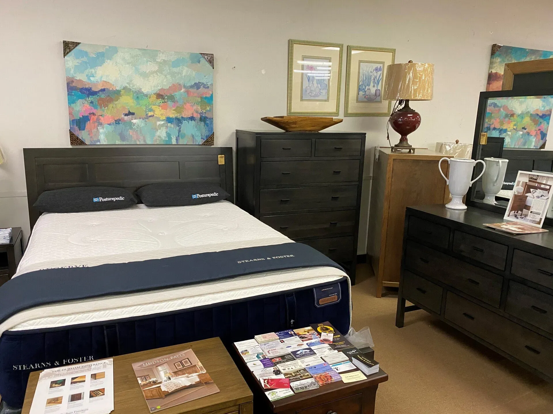 A bedroom furniture set featuring a dark wood bed frame, tall chest of drawers, dresser with mirror, and decorative art.