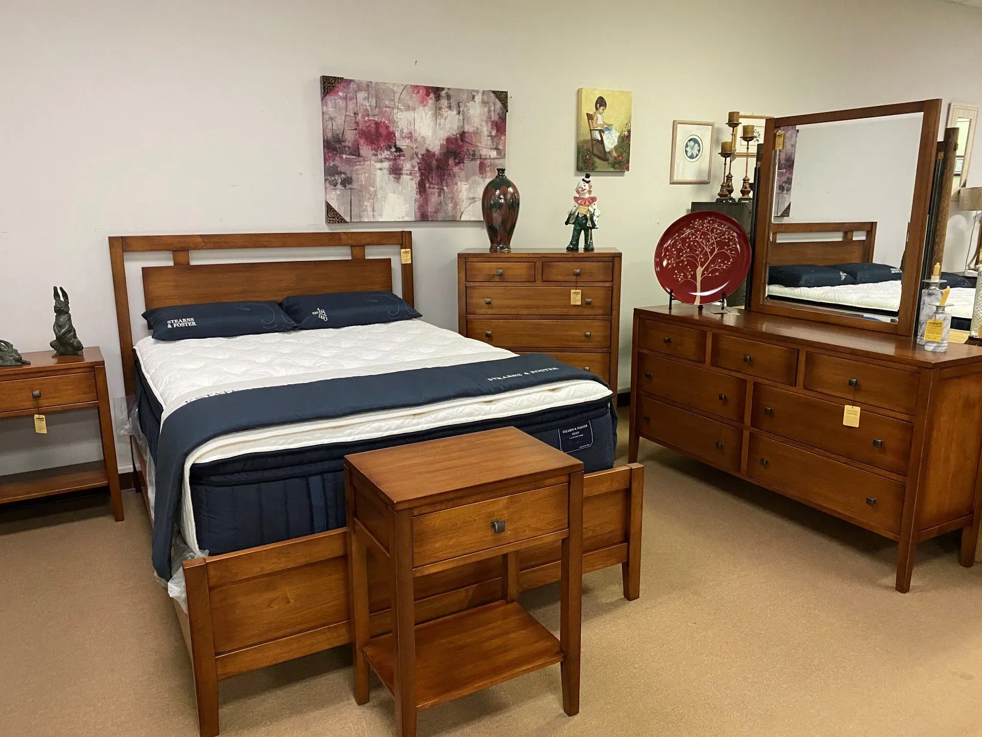 A bedroom furniture set featuring a wooden bed, a nightstand, a tall dresser, and a long dresser with a mirror.