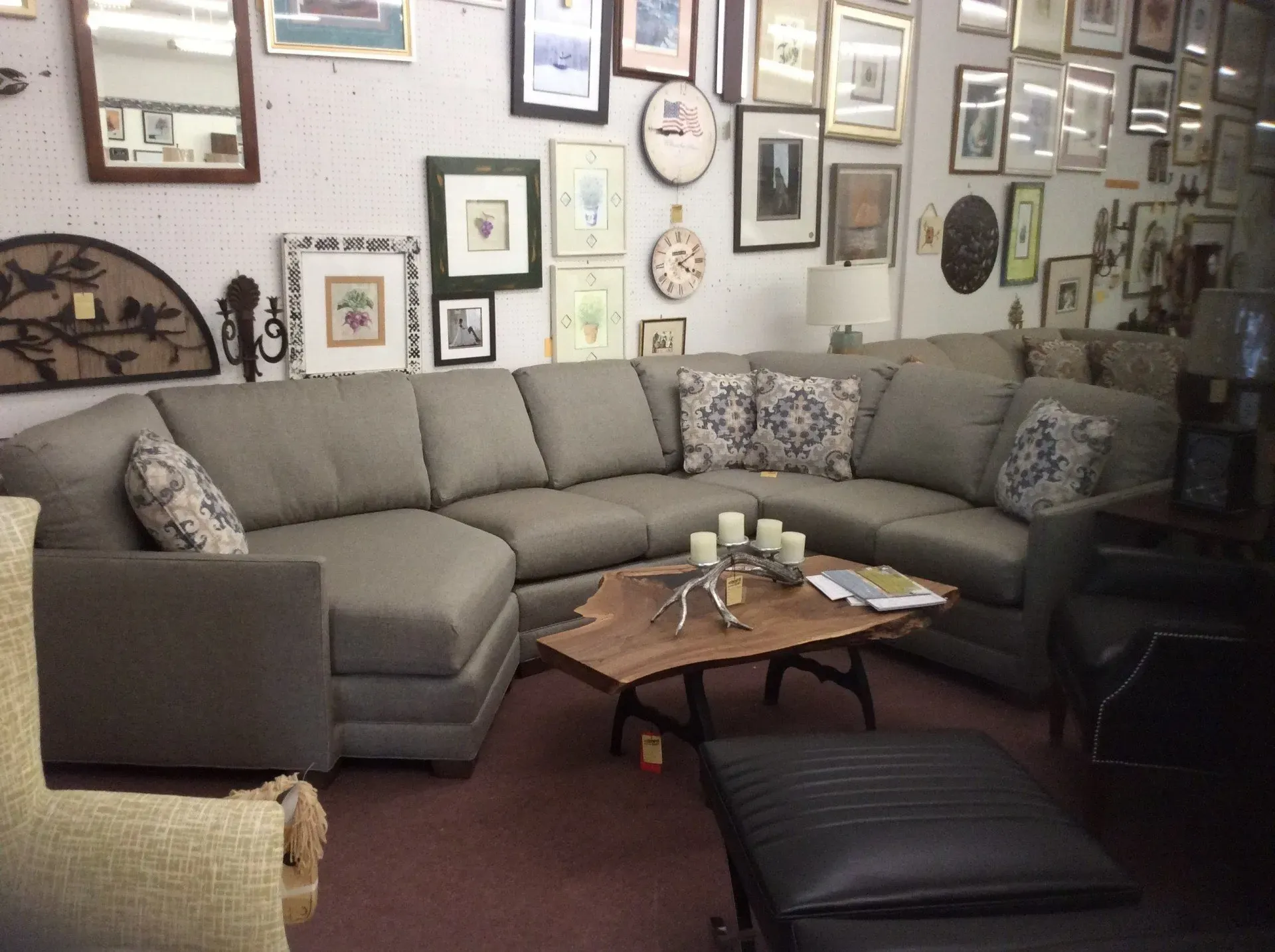 A grey sectional sofa sits in a room with a wood coffee table, an ottoman, and walls covered in various framed pictures.