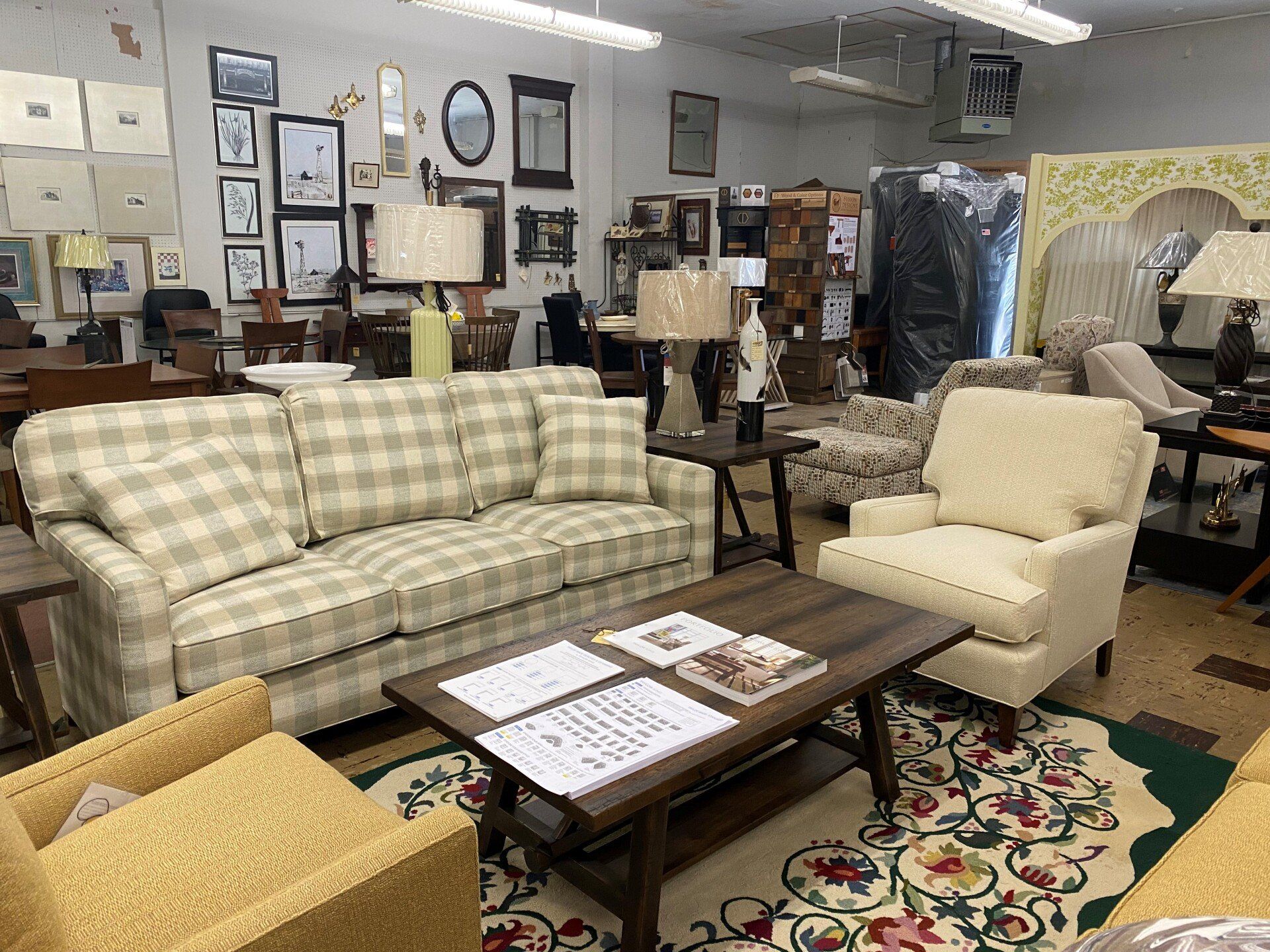 A living room showroom features a plaid sofa, a light-colored armchair, a wooden coffee table, and various home decor.