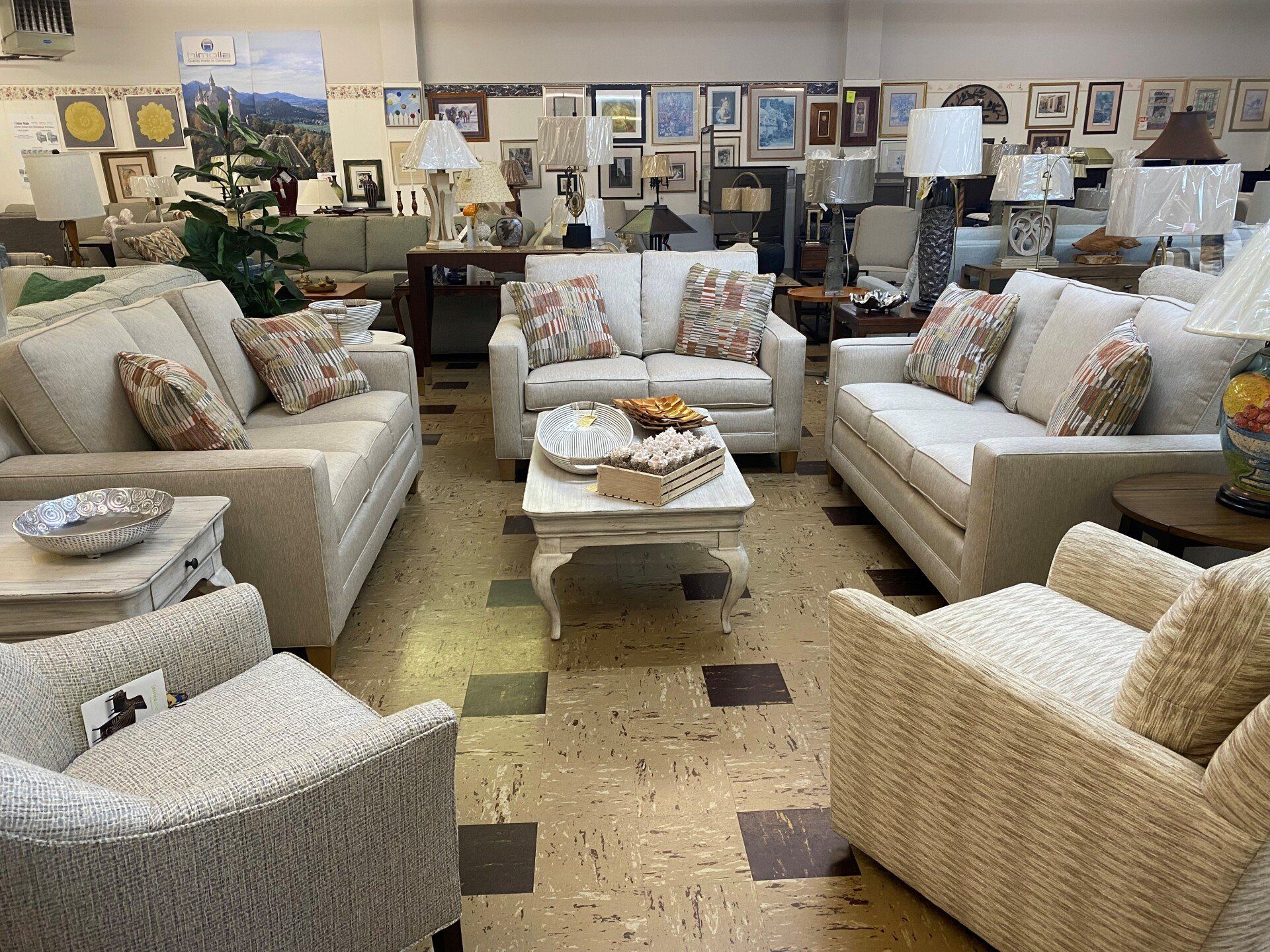 A furniture store showroom featuring three cream-colored sofas and two armchairs arranged around a central coffee table.