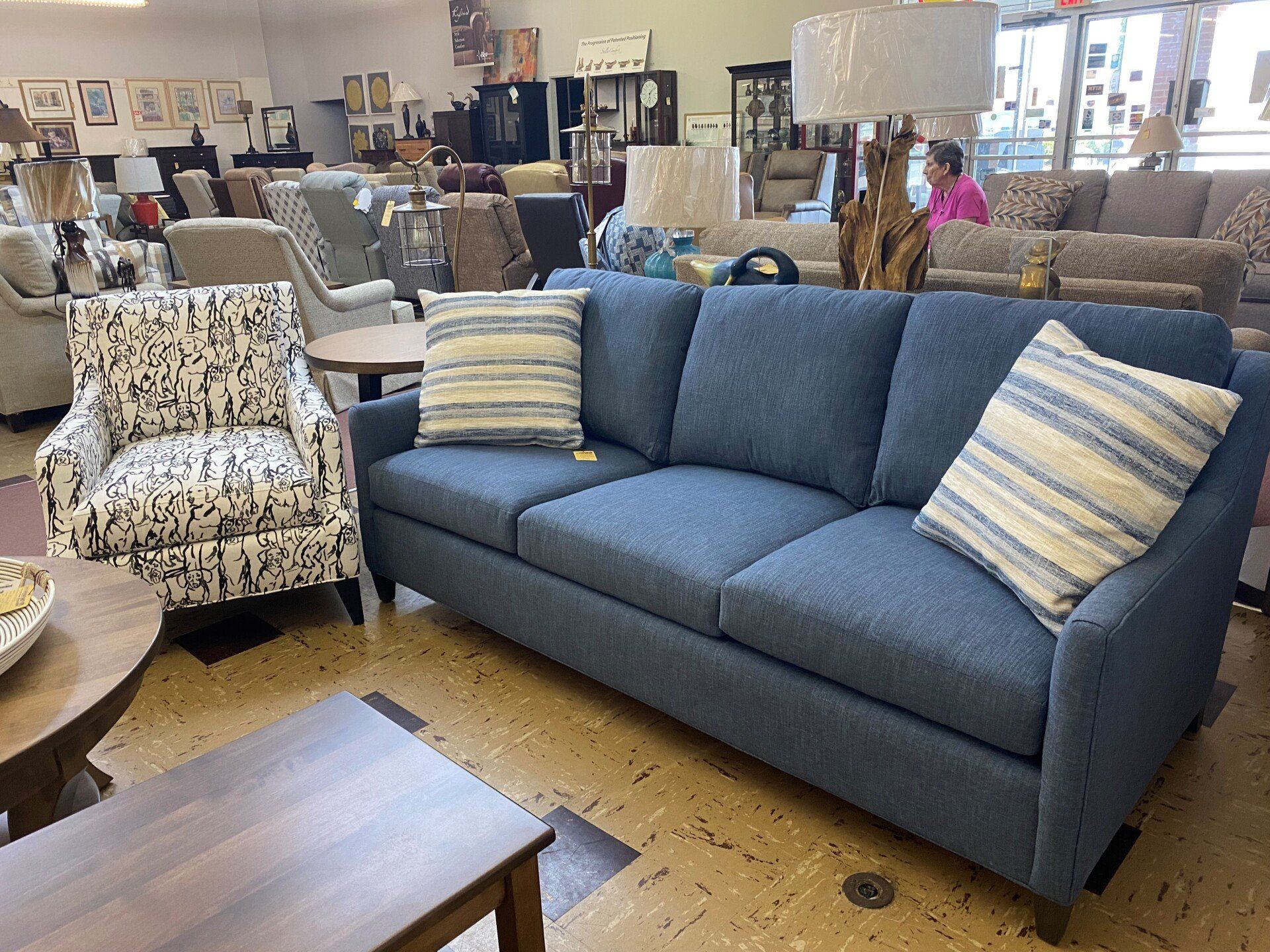 A showroom featuring a blue sofa with striped pillows next to a patterned armchair and wooden tables on a speckled floor.