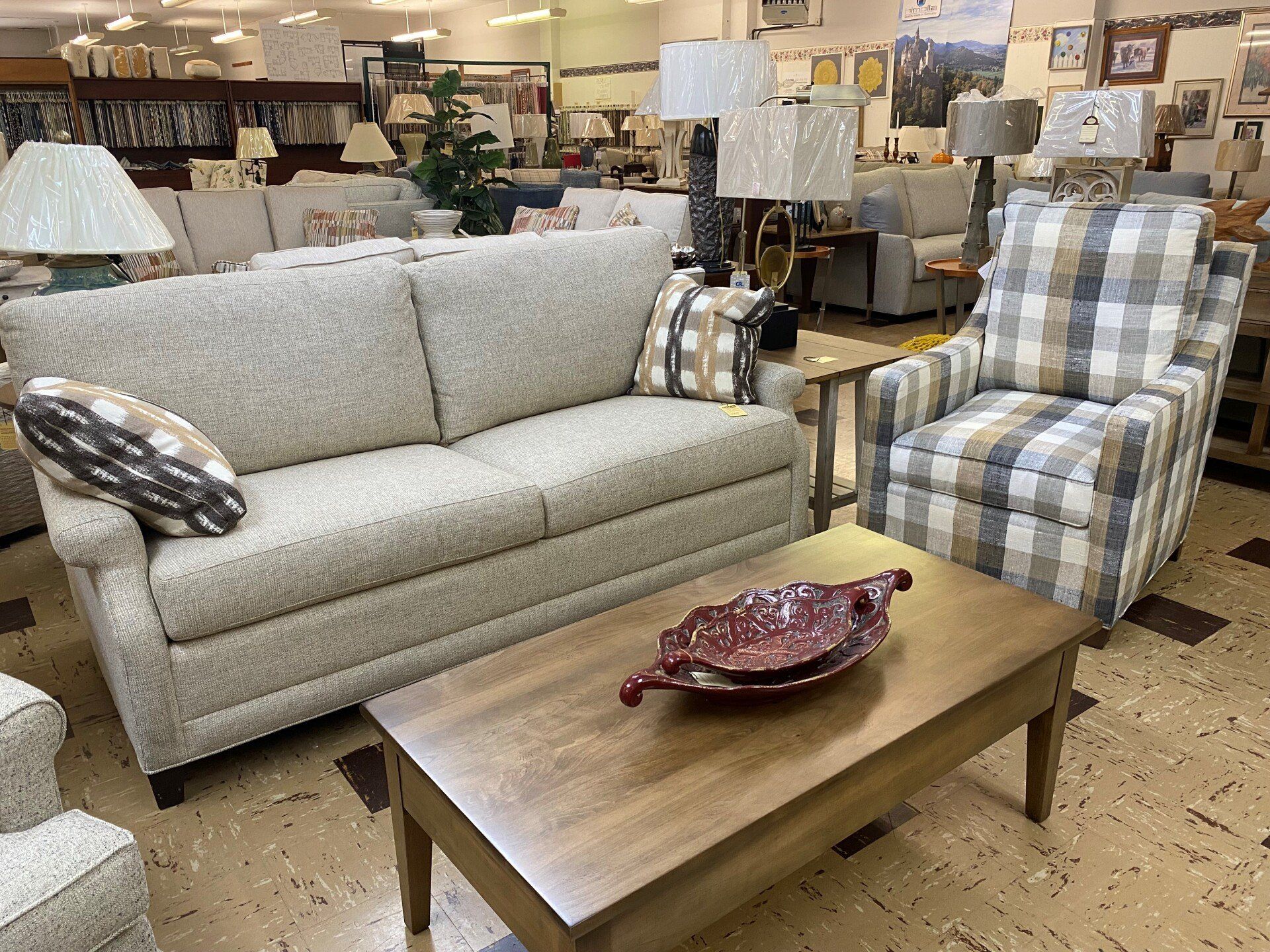 A beige sofa and a plaid armchair arranged around a wooden coffee table with a decorative bowl in a furniture store.