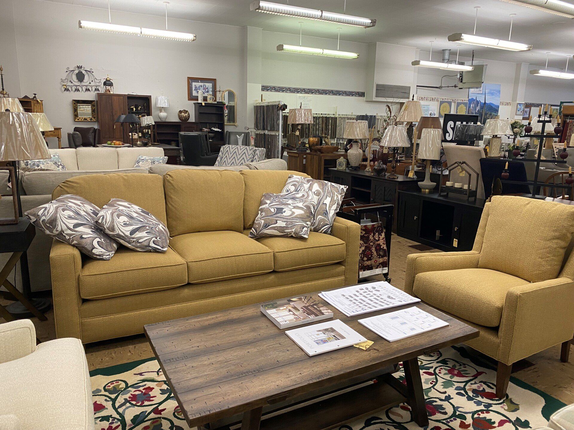 A furniture showroom featuring a yellow sofa and matching armchair arranged around a wooden coffee table on a rug.