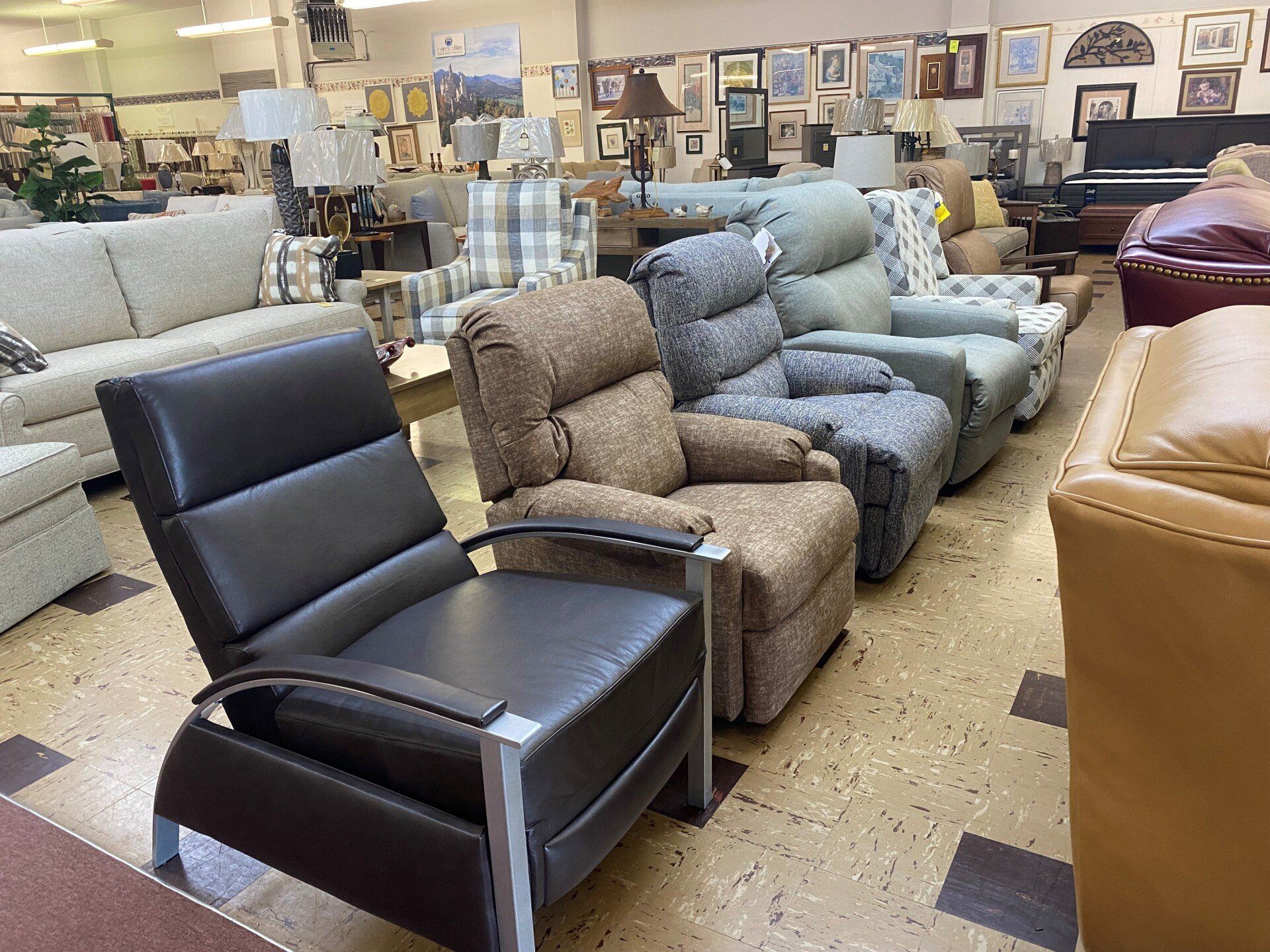 A showroom floor features a row of various recliners, including black, brown, and patterned fabric options.