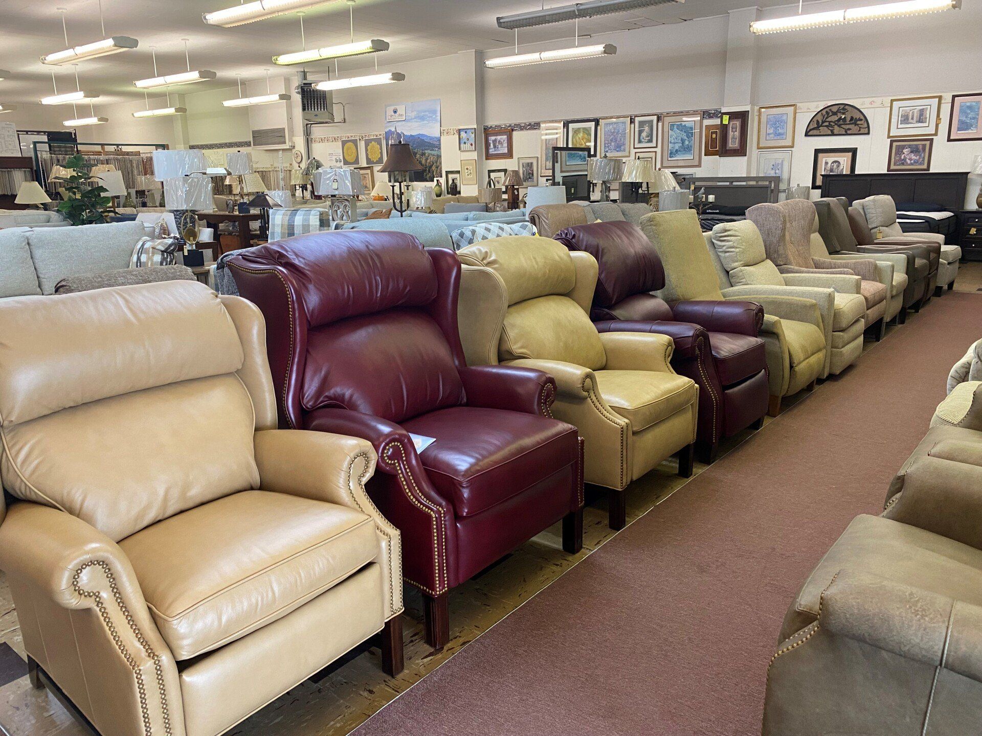A showroom floor displaying a row of leather recliners in shades of tan and burgundy, with furniture visible in the rear.