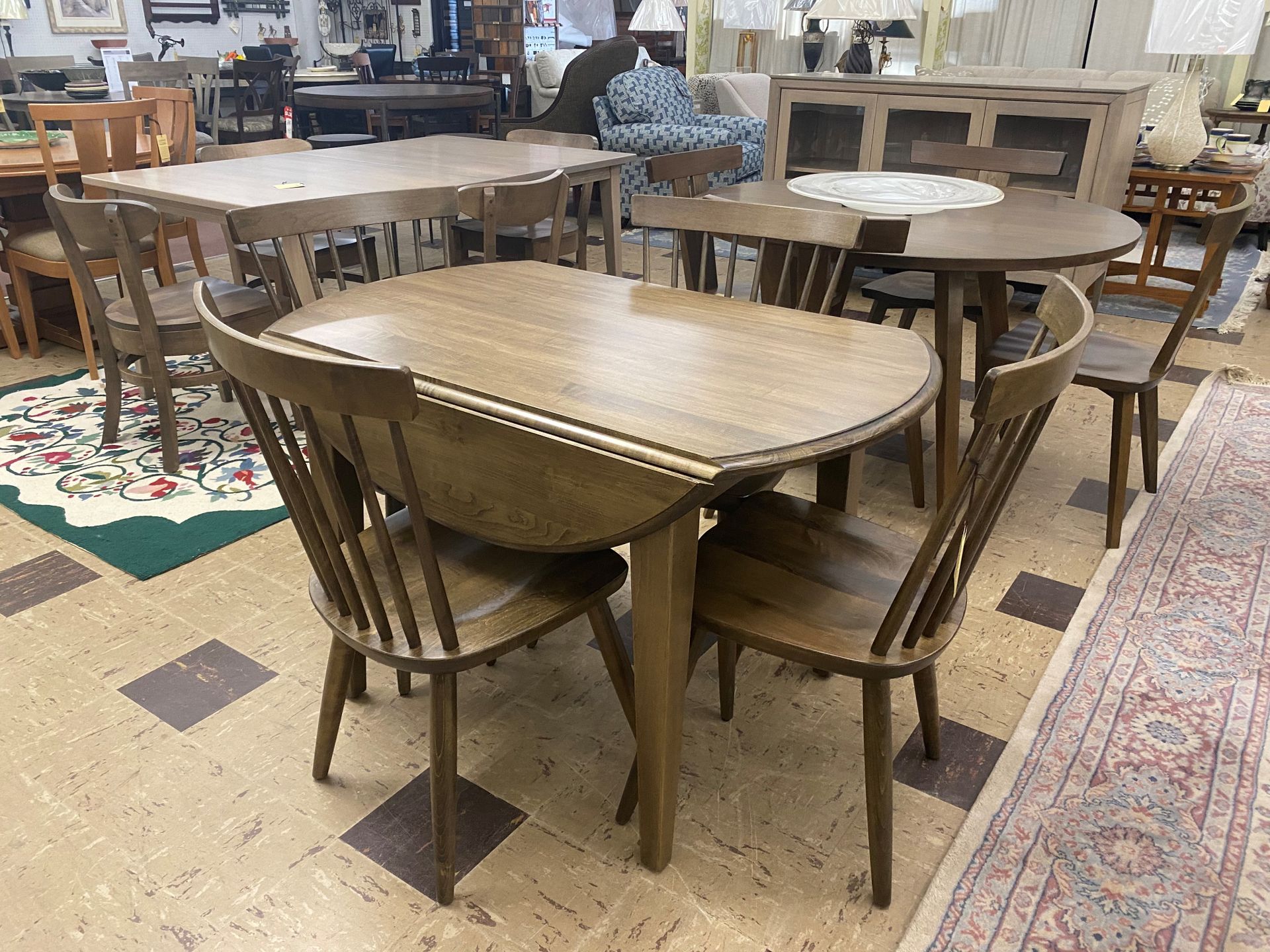 A store showroom display featuring light-wood drop-leaf tables and matching spindle-back chairs on a tiled floor.