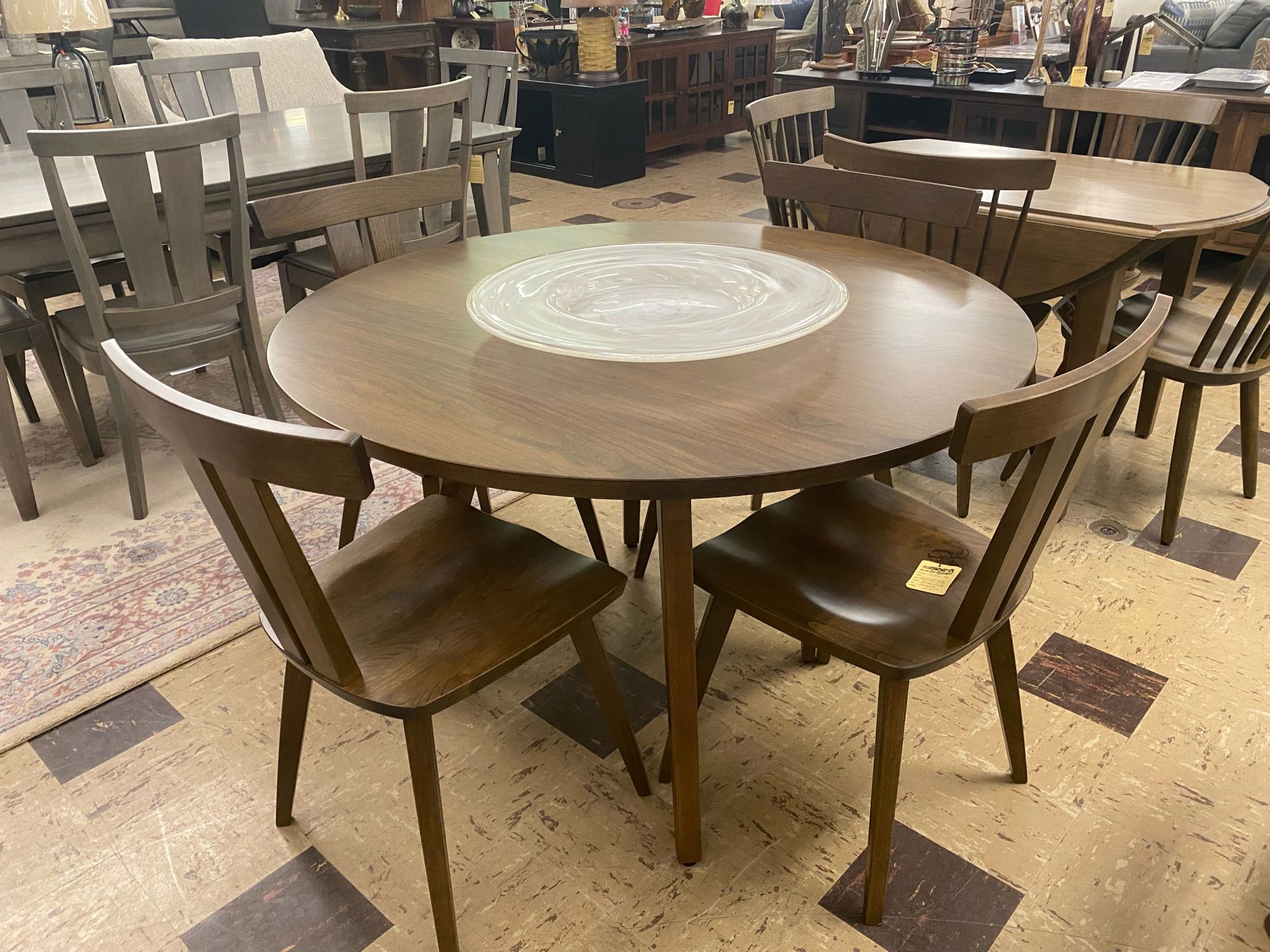 A round, dark wood dining table with four matching chairs in a furniture store showroom with tiled flooring.